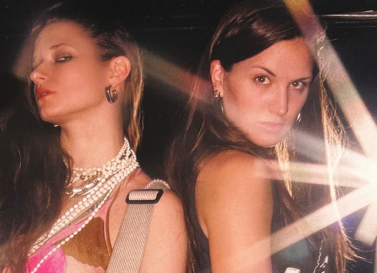 Two women pose confidently under stage lights in a dark setting.